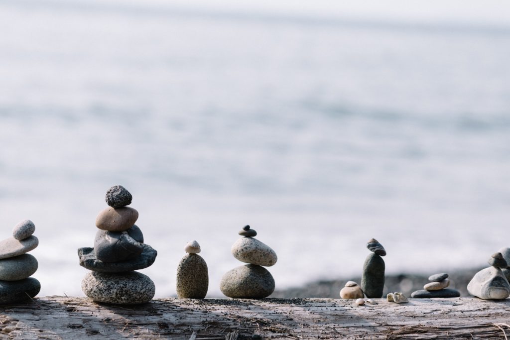 pebbles balanced on a driftwood trunk facing the sea, illustrating the balance between supply and demand, capacities and resources balanced with supply planning software