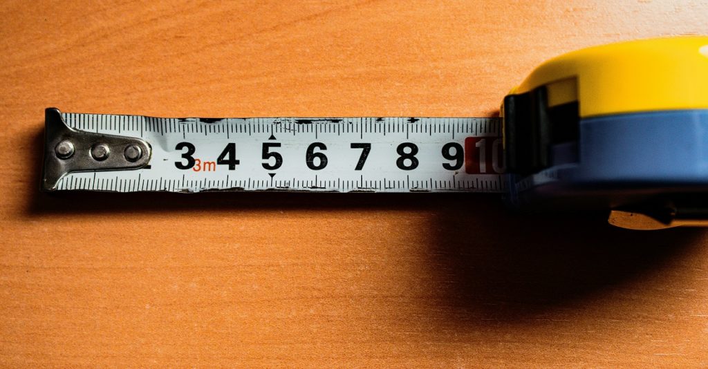 Définition du Contrôle de la qualité - Quality Control – QC illustré par un mètre ruban sur une table en bois_mark-owen-wilkinson-hughes