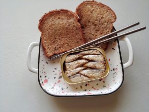 boite de sardines et tranches de pain sur un plat avec paire de baguettes illustrant DLUO vs DLC
