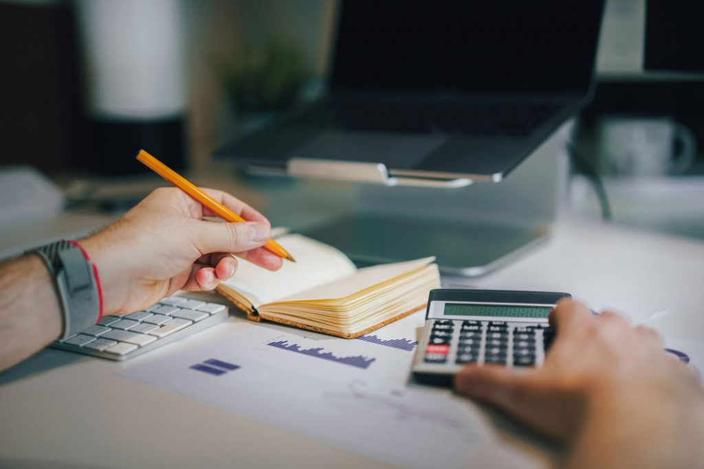 les mains d'une personne avec calculatrice et carnet de notes illustrant les b&eacute;n&eacute;fices concrets du S&OP
